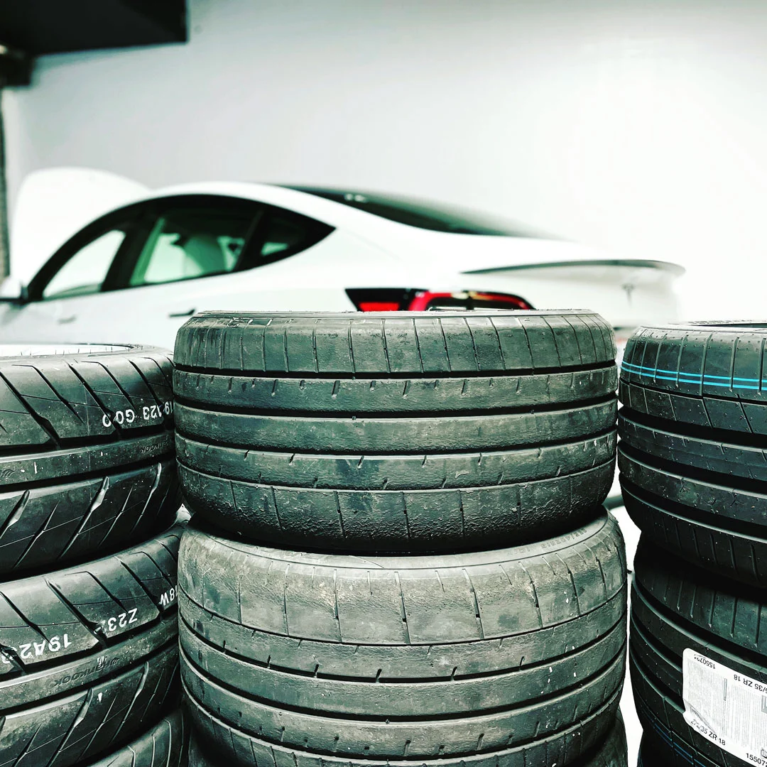 Stacks of tires behind a Tesla Model 3.
